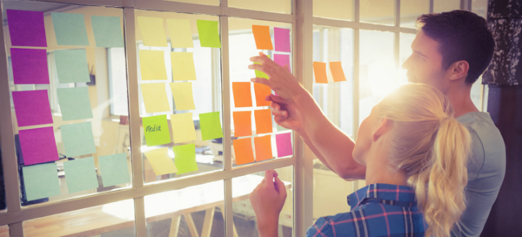 Jovens discutem ideias colando post-its em parede de vidro