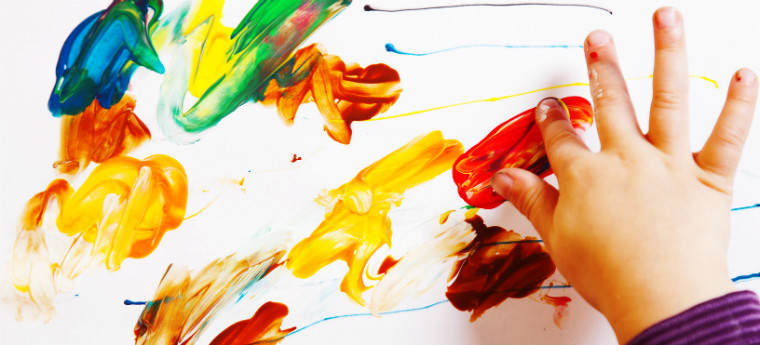 Criança pinta folha em branco usando os dedos