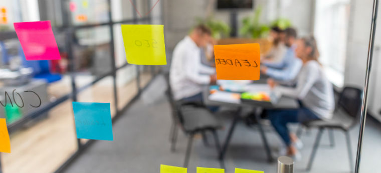 AGITA Edtech - Jovens empreendedores reunidos para uma reunião são vistos em uma sala de vidro com post-its colados nas paredes