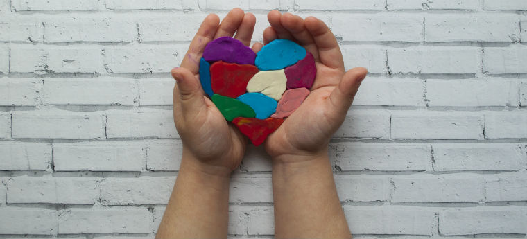 Mãos de criança segurando um coração multicolorido em fundo branco