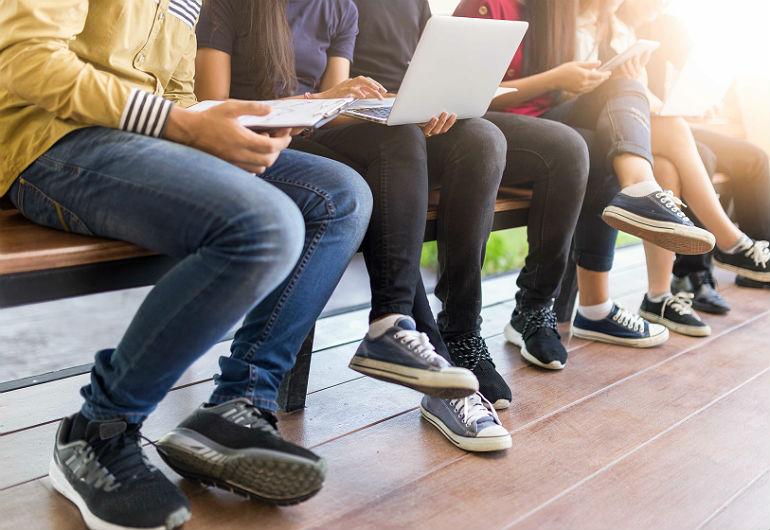 Estudantes sentados em um banco usando computador