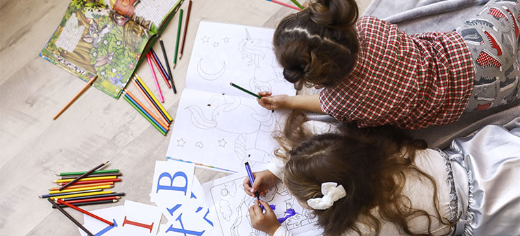 Duas crianças lendo e desenhando no chão
