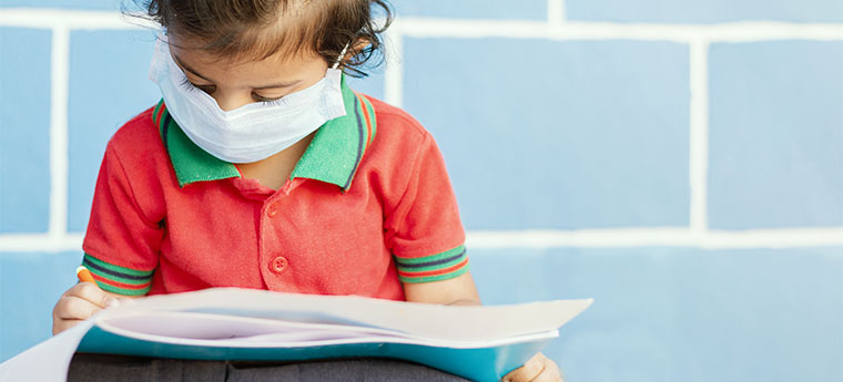 Menina usando máscara lê livro sentada