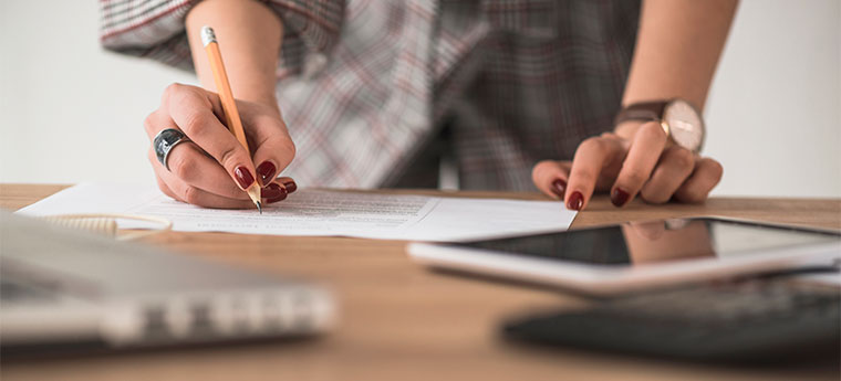 Mulher escreve em papel sobre uma mesa com tablet e computador