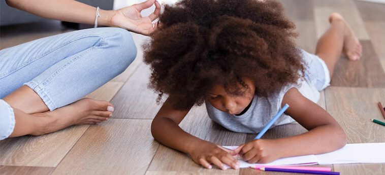 Menina negra desenha no chão enquanto a mãe medita