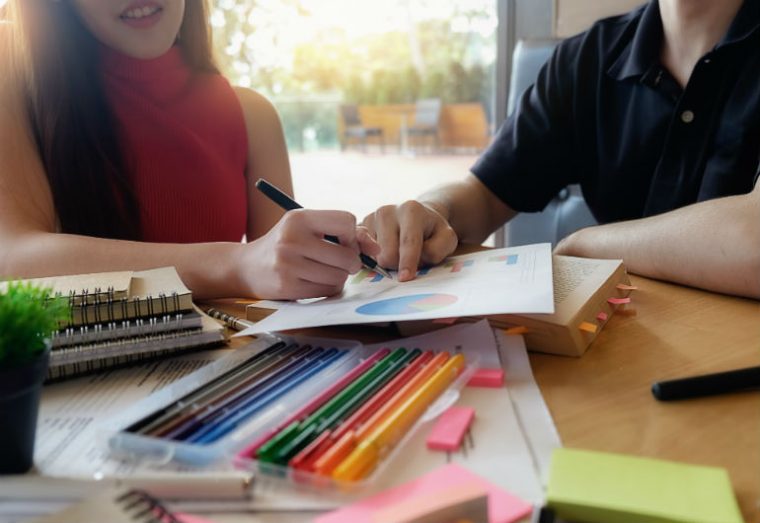Jovens discutem projeto em uma mesa com relatórios e lápis coloridos