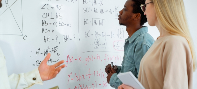 Grupo de três pessoas discutindo equações matemáticas em um quadro branco.