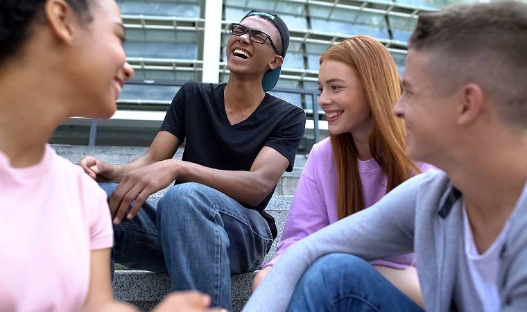 Grupo de quatro jovens sentados em escada ao ar livre, rindo e conversando.