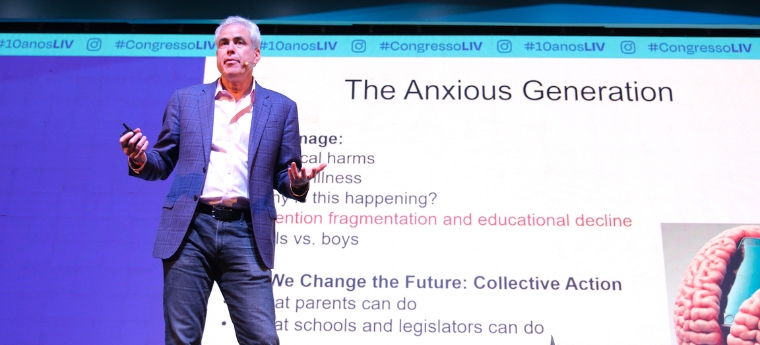 Palestrante apresenta o tema “The Anxious Generation” diante de um slide com tópicos sobre saúde mental e juventude.