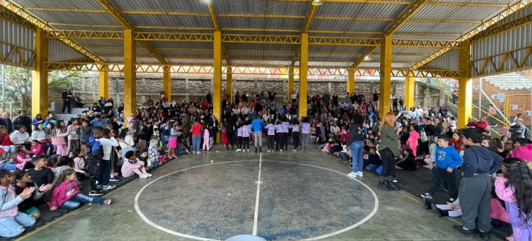 Ginásio cheio de crianças e adultos assistindo a uma apresentação.