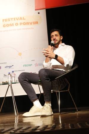 David Almansa, homem de camisa branca e tênis claros falando no palco do Festival Encontro com o Porvir.