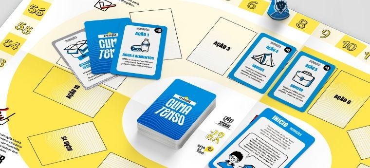 Foto do tabuleiro e cartas do jogo “Clima Tenso”, com peças e trilha numerada.