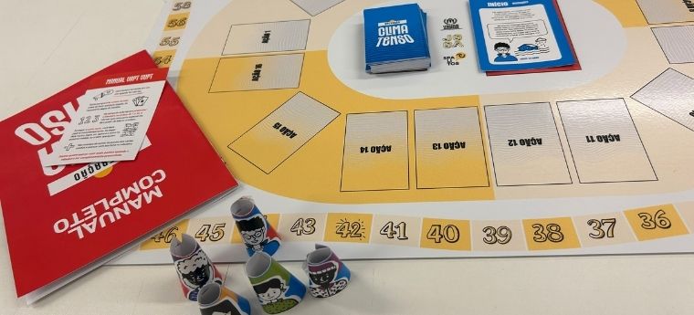 Imagem do jogo “Clima Tenso” com tabuleiro, manual e pinos com personagens ilustrados.
