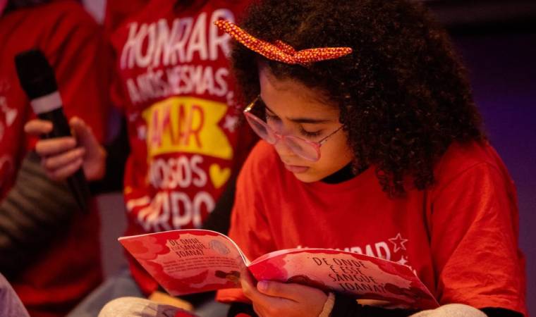 Menina lê livro sobre menstruação e educação corporal, com camiseta do projeto 'Honrar a nós mesmas'.