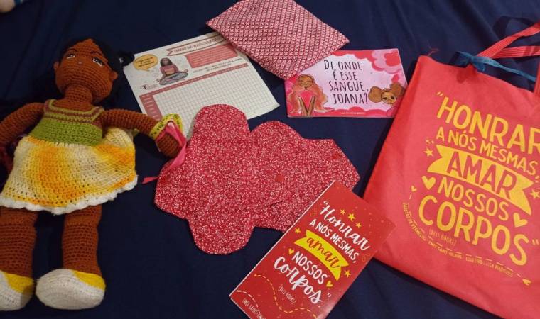 Kit educativo com livro, absorventes de pano, cartilha e boneca, voltado à educação menstrual e autoestima.