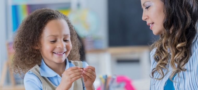 Criança e professora brincando com blocos coloridos em sala de aula.