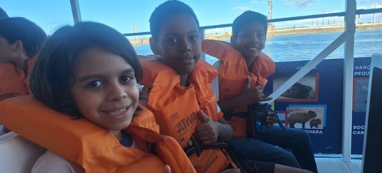 Crianças com coletes salva-vidas sorrindo em um passeio de barco.