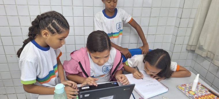 Grupo de meninas trabalhando juntas com notebook e caderno em sala de aula.
