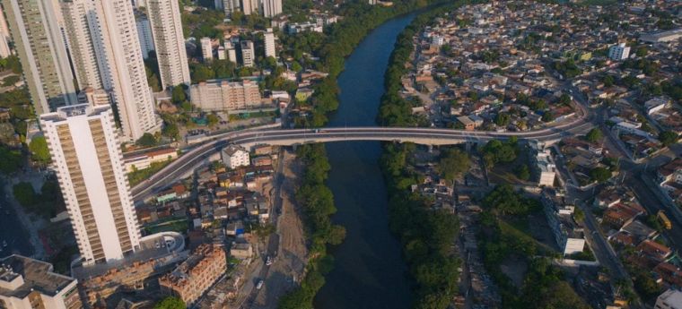 Vista aérea de cidade com rio central e ponte ligando áreas urbanas.