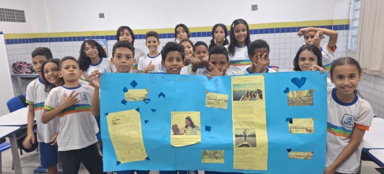 Turma de alunos apresenta cartaz azul com textos e imagens colados.