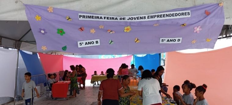 Evento escolar com a faixa “Primeira Feira de Jovens Empreendedores”, com bancas organizadas por alunos do 5º ano.