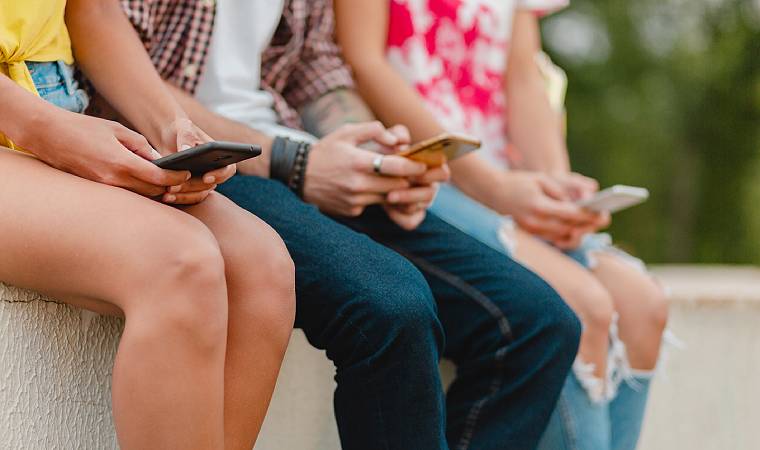 Quatro pessoas sentadas lado a lado usando celulares, vistas da cintura para baixo.