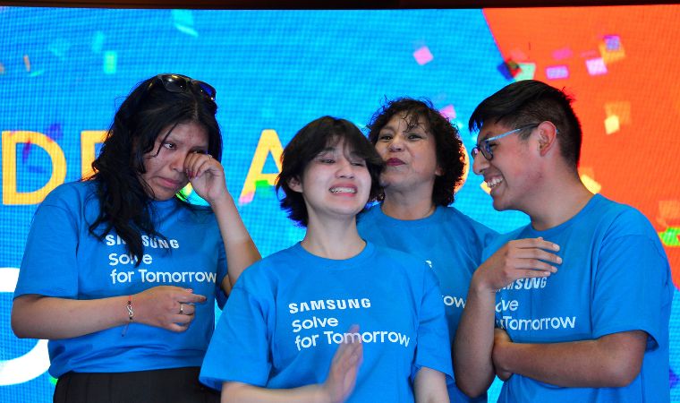 Jovens com camisetas azuis da Samsung comemoram emocionados em um palco colorido.