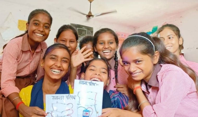 Meninas escolares sorrindo e segurando cartazes em sala de aula.
