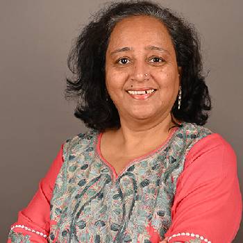 Retrato de mulher sorridente com blusa estampada, em fundo neutro.