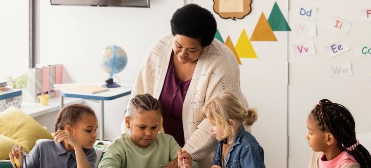 Professora acompanha grupo de quatro crian&ccedil;as desenhando em sala de aula