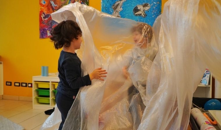 Duas crianças brincam atrás de uma grande folha de plástico transparente