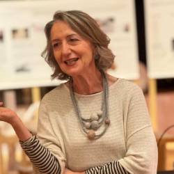 Mulher sorri e gesticula em frente a painéis expositivos