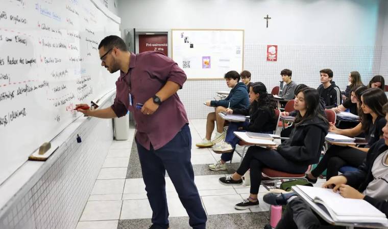 Professor escreve no quadro branco enquanto alunos observam e anotam