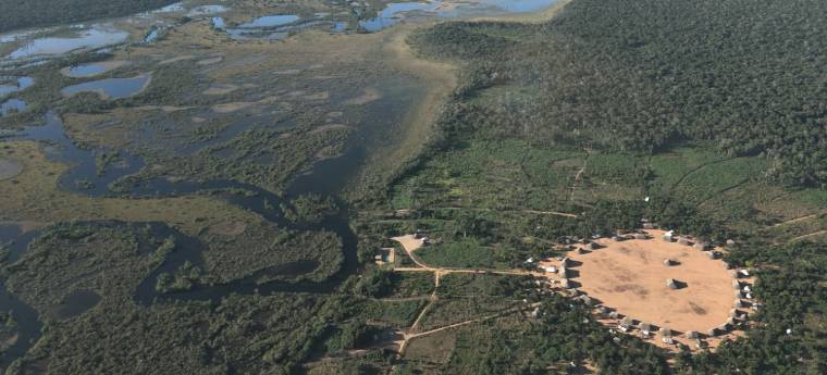 Aldeia indígena circular cercada por floresta e áreas alagadas
