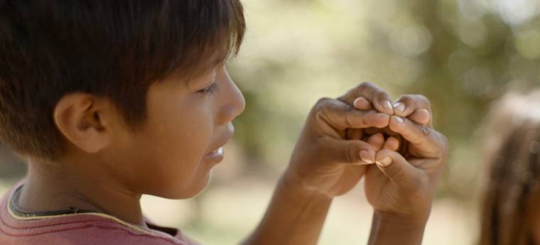 Menino observa atentamente gesto feito com as mãos