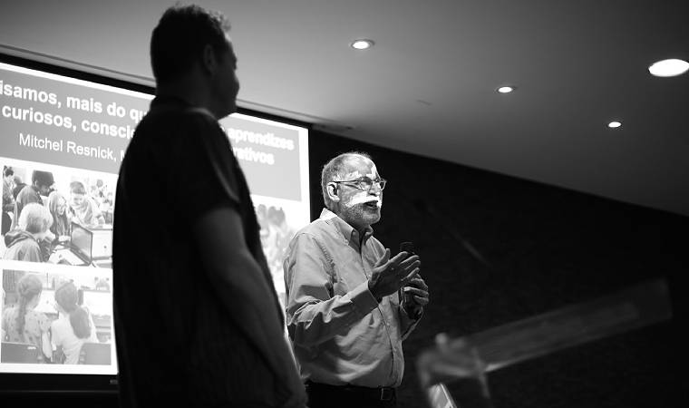 Mitchel Resnick fala ao público durante palestra com slide projetado ao fundo