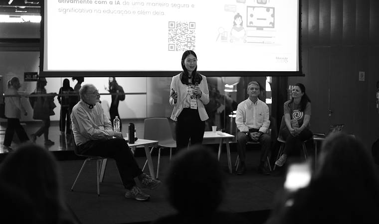 Natalie Lao fala em pé durante painel com Mitchel Resnick e outros convidados, com slide sobre IA na educação ao fundo