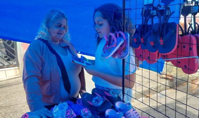 Criança conversa com vendedora de calçados infantis em feira livre