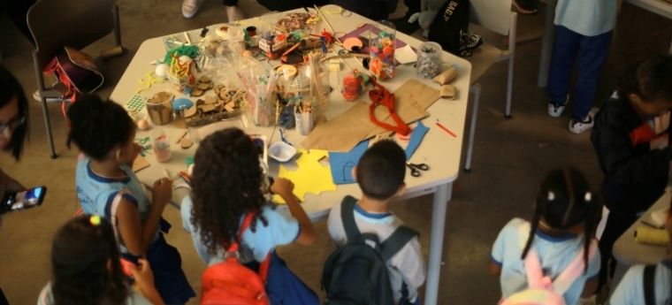 Crianças em pé ao redor de uma mesa com materiais de artesanato
