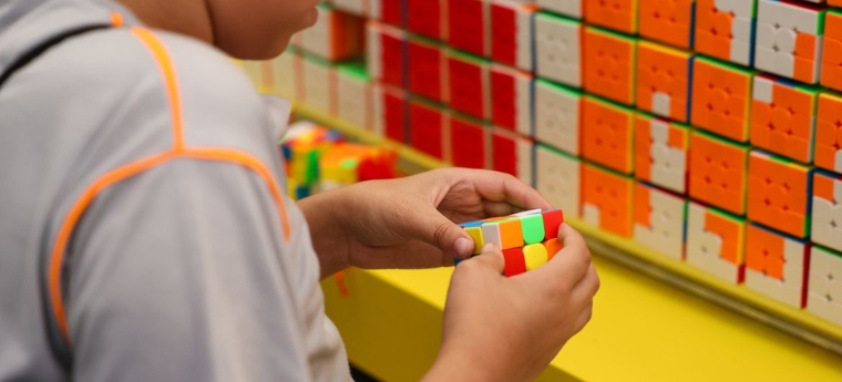Criança segurando um cubo mágico colorido, com várias peças empilhadas ao fundo