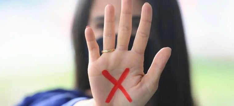 Mulher mostra palma da mão com um X vermelho pintado, sinal de pedido de socorro contra violência