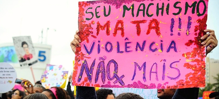 Manifestante segura cartaz rosa com a frase "Seu machismo mata!!! Violência não mais"