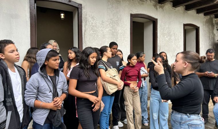 Mulher faz explicação a grupo de estudantes em pátio colonial