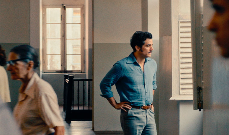 Homem em pé no corredor de prédio antigo, olhando para fora