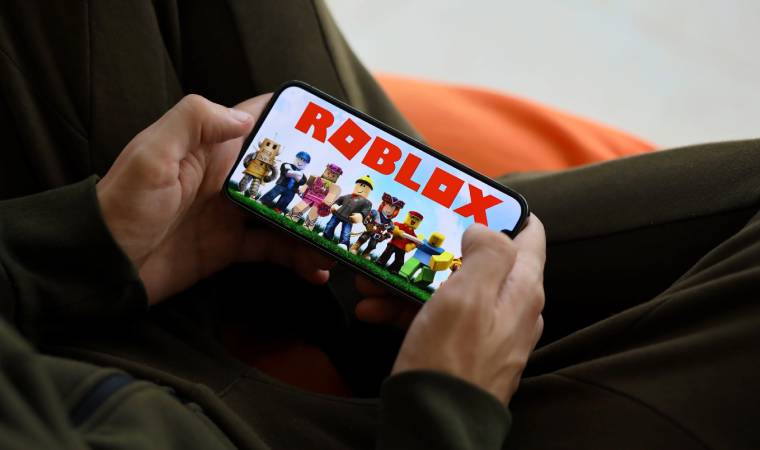 Tela de celular exibindo o jogo Roblox, segurado por uma pessoa sentada