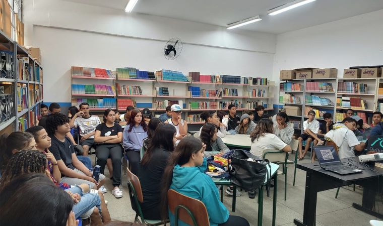Grupo de estudantes sentados em círculo em uma biblioteca escolar