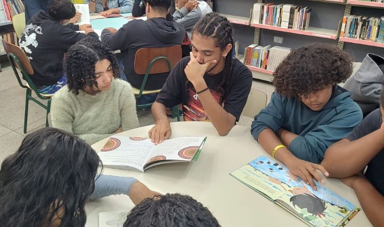 Grupo de adolescentes lê livros ilustrados juntos em mesa redonda