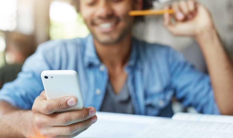 Homem segura smartphone e sorri com livro aberto à frente