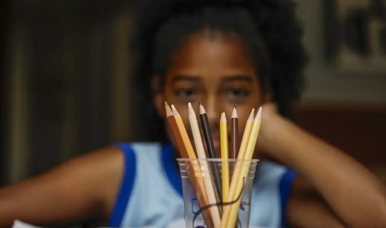 Crian&ccedil;a observa copo com l&aacute;pis de cor organizados sobre a mesa